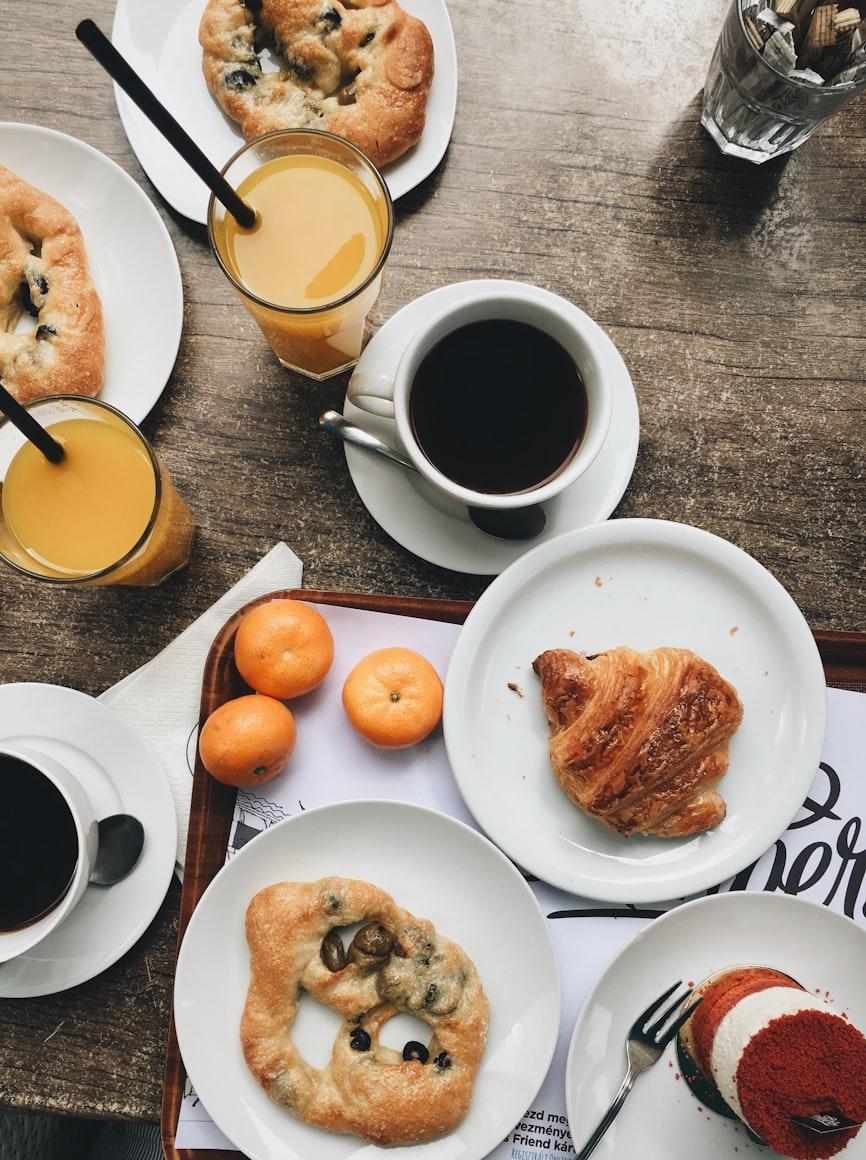 A brunch spread of fresh pastries, espresso, orange juice and mandarins on a wooden table