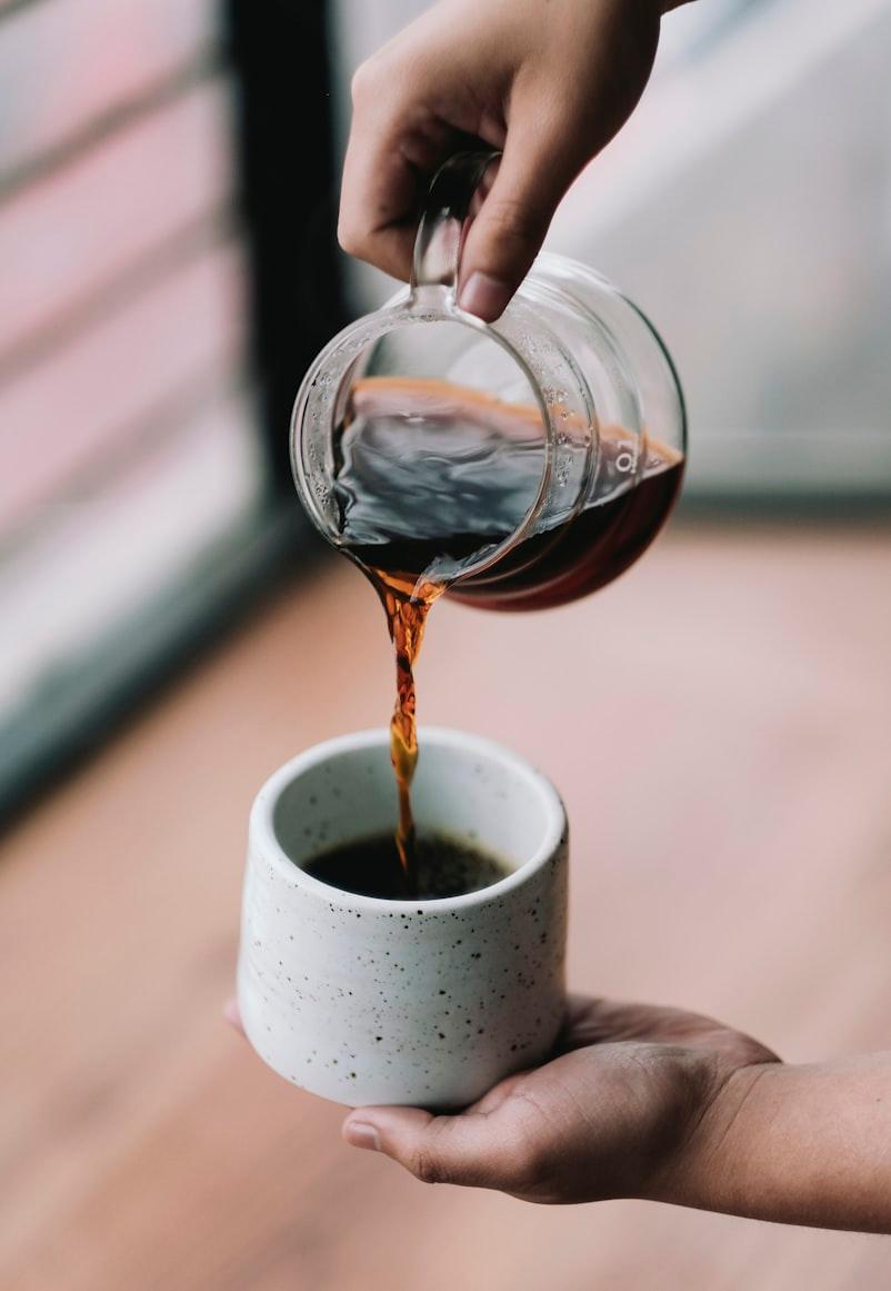 Hands carefully pouring filter coffee from a carafe into a stoneware cup