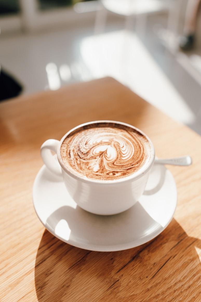 A single cappuccino with swirled latte art on a sunlit timber table