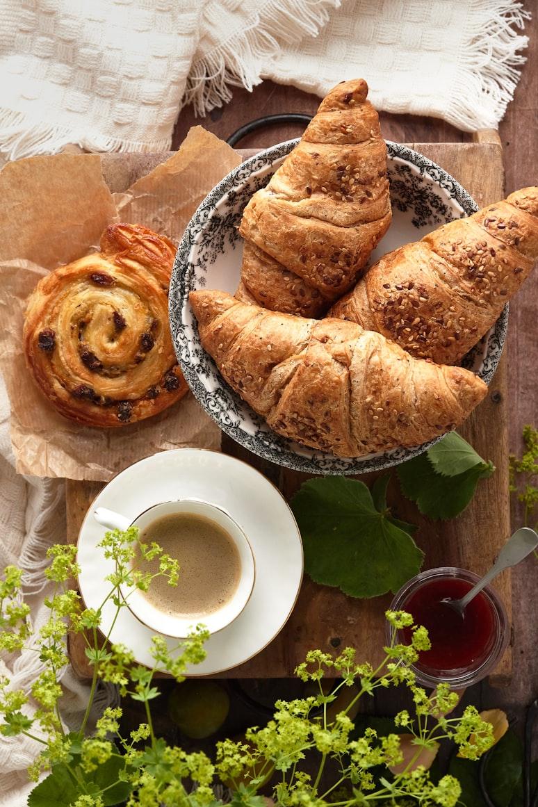 Multigrain croissants and a sweet pastry on a vintage plate with espresso and jam, dressed with fresh herbs