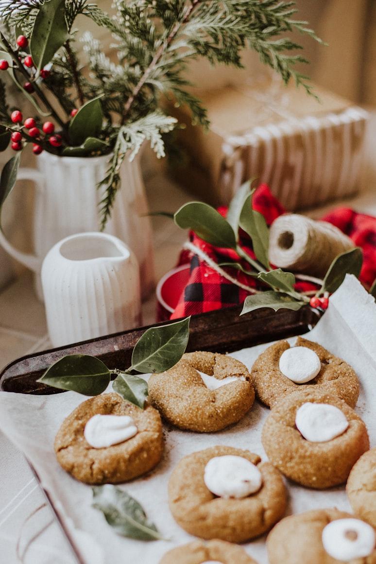 Soft ginger cookies topped with marshmallow on parchment, beside winter foliage