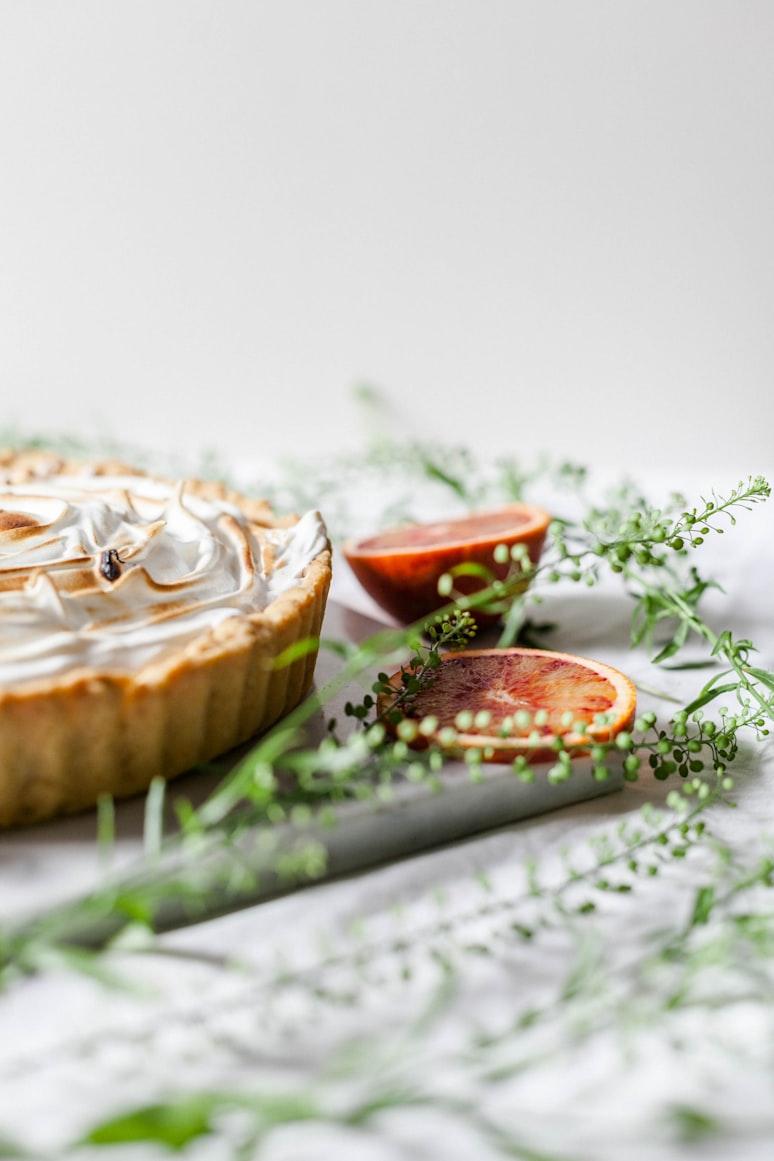 A blood-orange meringue tart on a marble board with trailing greenery