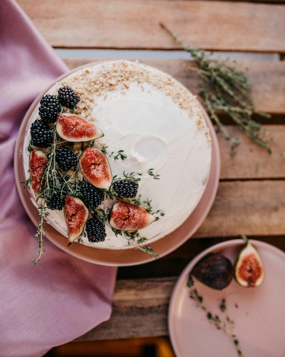 A naked layer cake topped with figs, blackberries and thyme on a wooden table