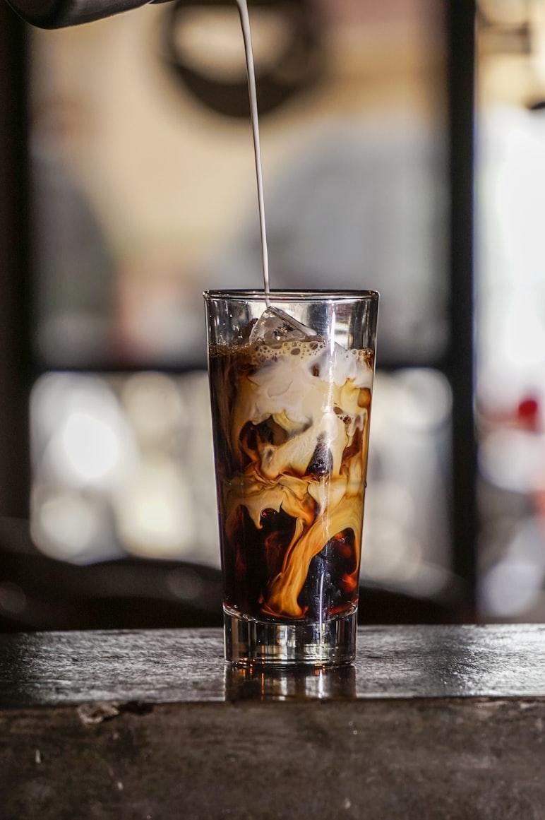 Iced coffee in a tall glass with cream being slowly poured in